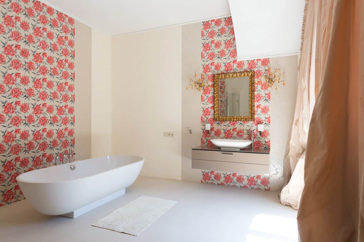 Bathroom interior with bold red floral peel and stick wallpaper on walls, freestanding bathtub and gold mirror